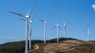 A group of wind turbines in a green pasture next to a winding pathway.